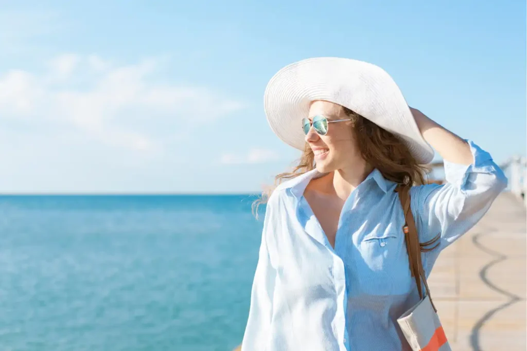 woman near the ocean with hat and sunglasses